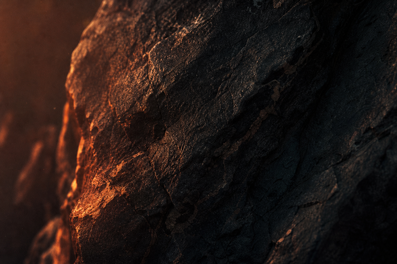 Macro view of weathered dark stone catching a low ember-coloured light along its grain.